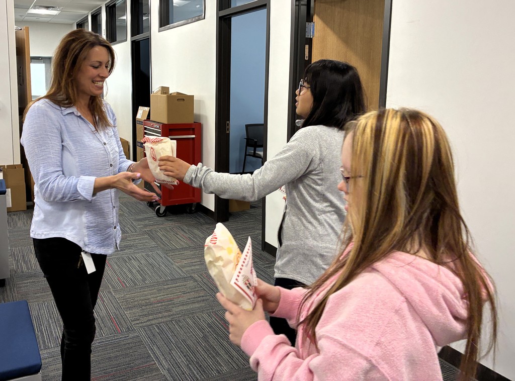Picture of  two students with a cart full of popcorn bags handing one out to a woman in an office