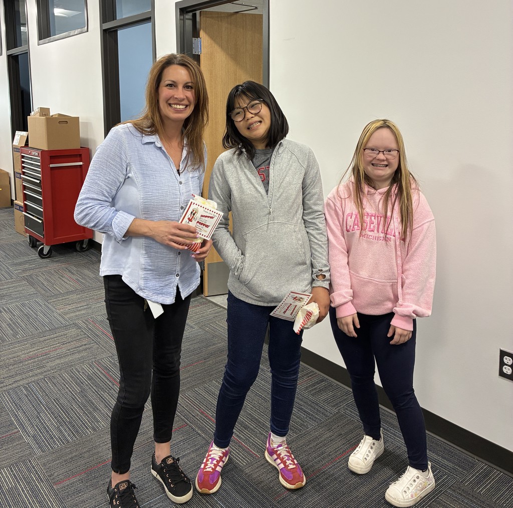 Picture of  two students with a cart full of popcorn bags handing one out to a woman in an office