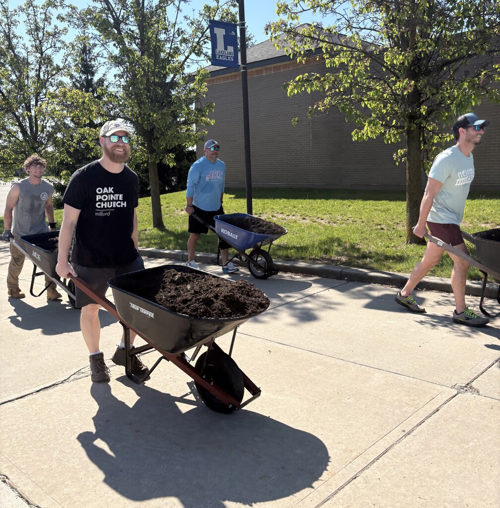 People using wheel barrels to halp clean up outside school