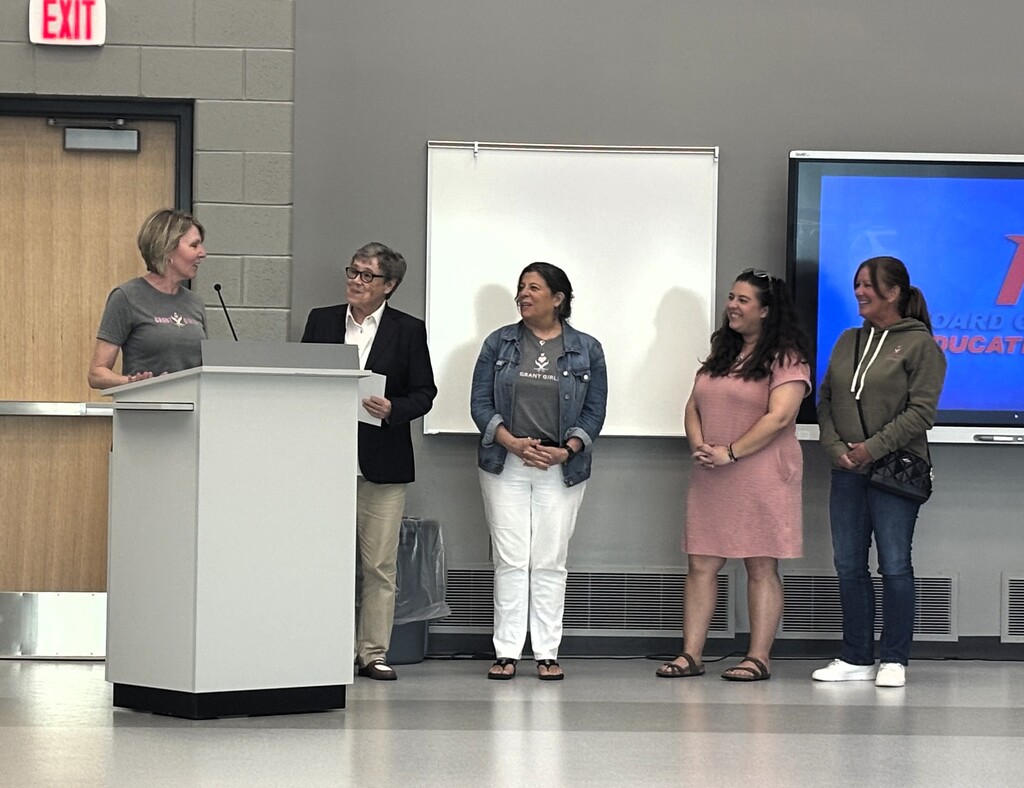 Grant Girls women & hvs board member listen to woman at podium as they receive honor for their service