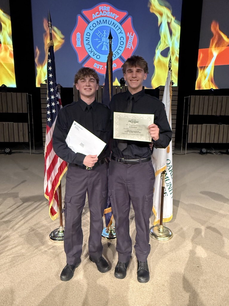 2 students with flags behind them holding certificates. 