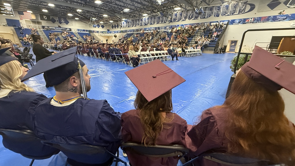 Photo of students sitting down wearing their cap & gown at a graduation ceremony. 