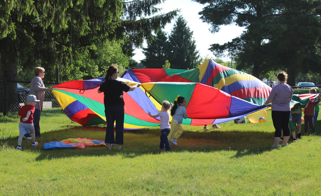 Photo of kids playing with parachute along with adults