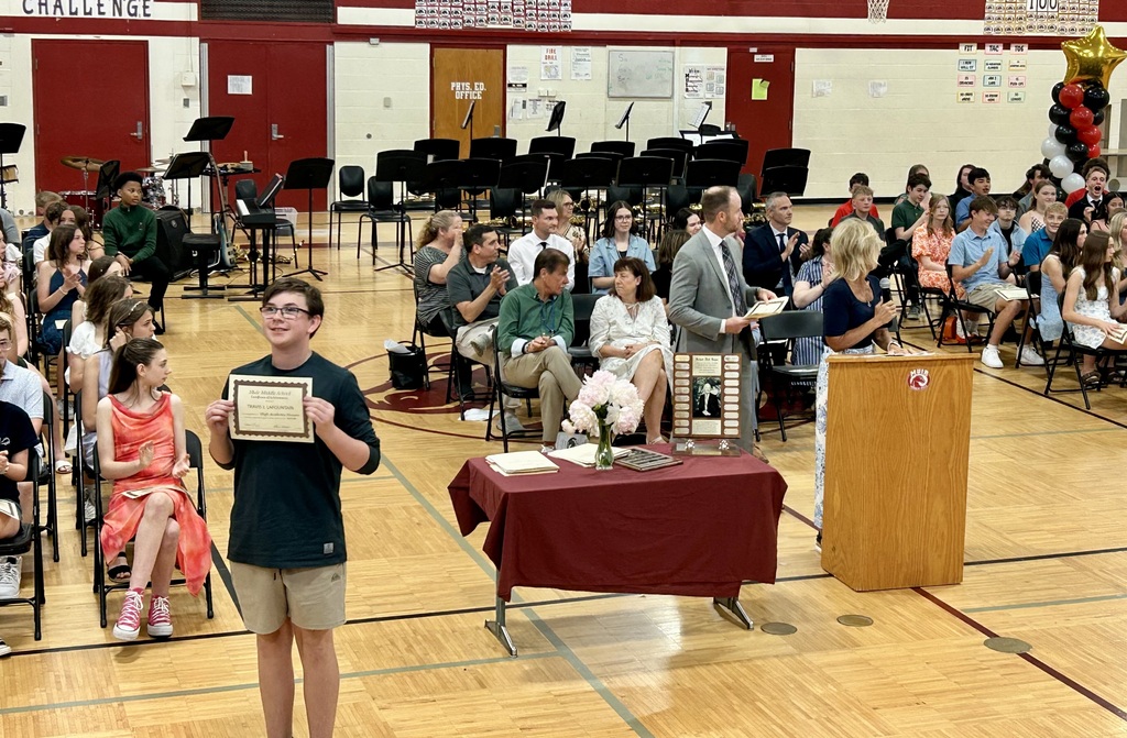 Student holding up certificate in front of school assembly for honors night