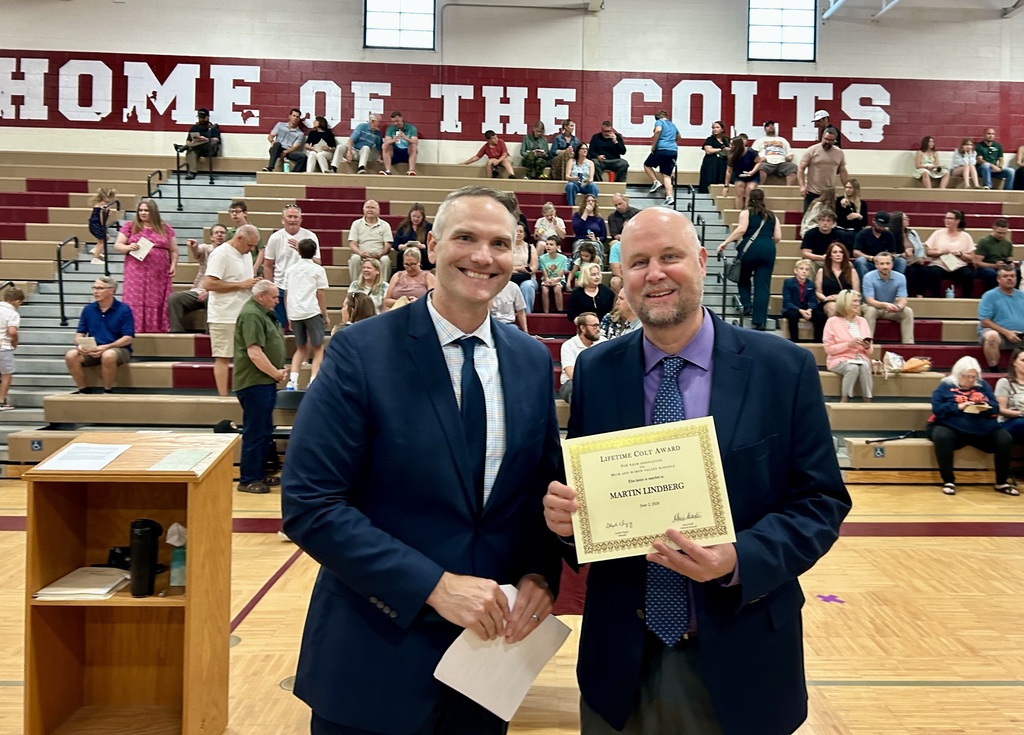 Two educators holding up certificate in front of school assembly for honors night