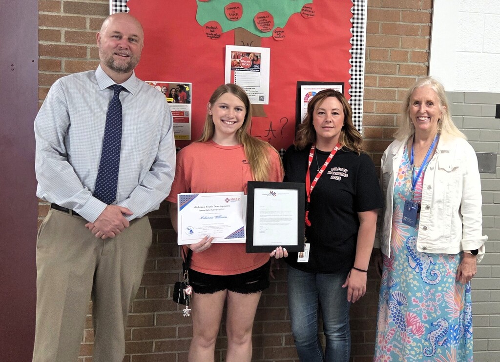 Student holding YDA certificate smiling and standing with three educators.