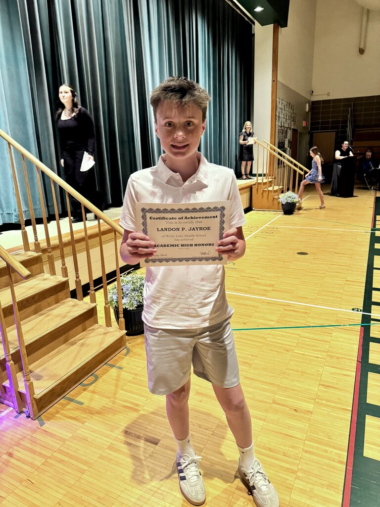 Student stands and holds up a certificate ont he gym floor during a ceremony