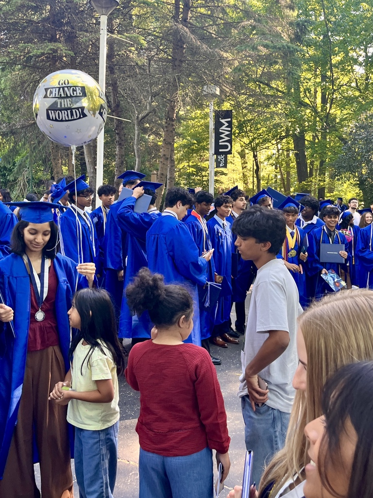 Photo of dozens of students in blue cap and gowns taking pictures at graduation