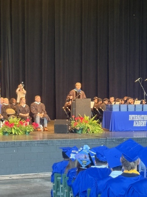 Educators on stage in grad gowns , man speaking at podium during graduation