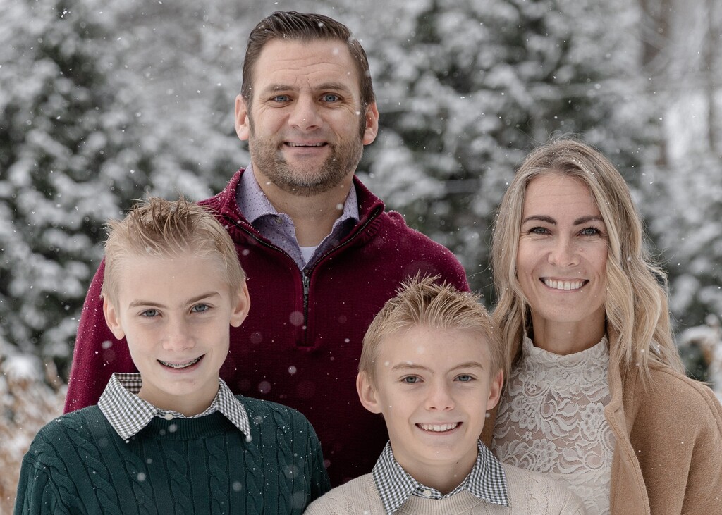 Photo of family of 4 posing outisde with snow falling and snow covered trees