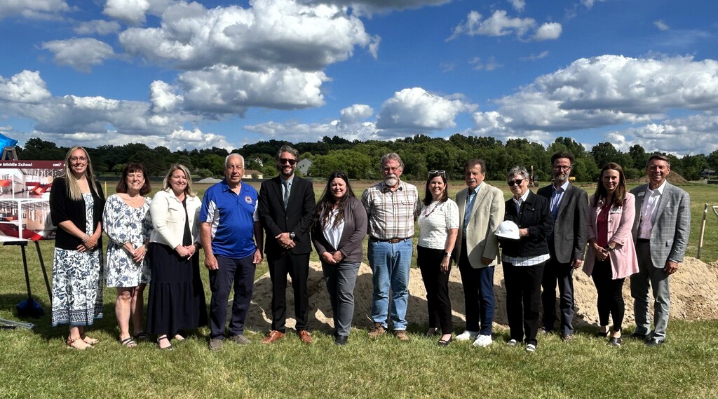 Photo of several people posing for a photo  standing in front of a mound of dirt