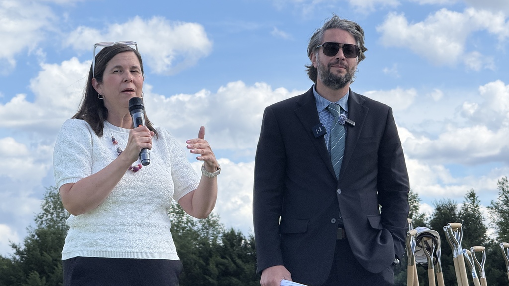 Photo of woman speaking into microphone while man next to her watches