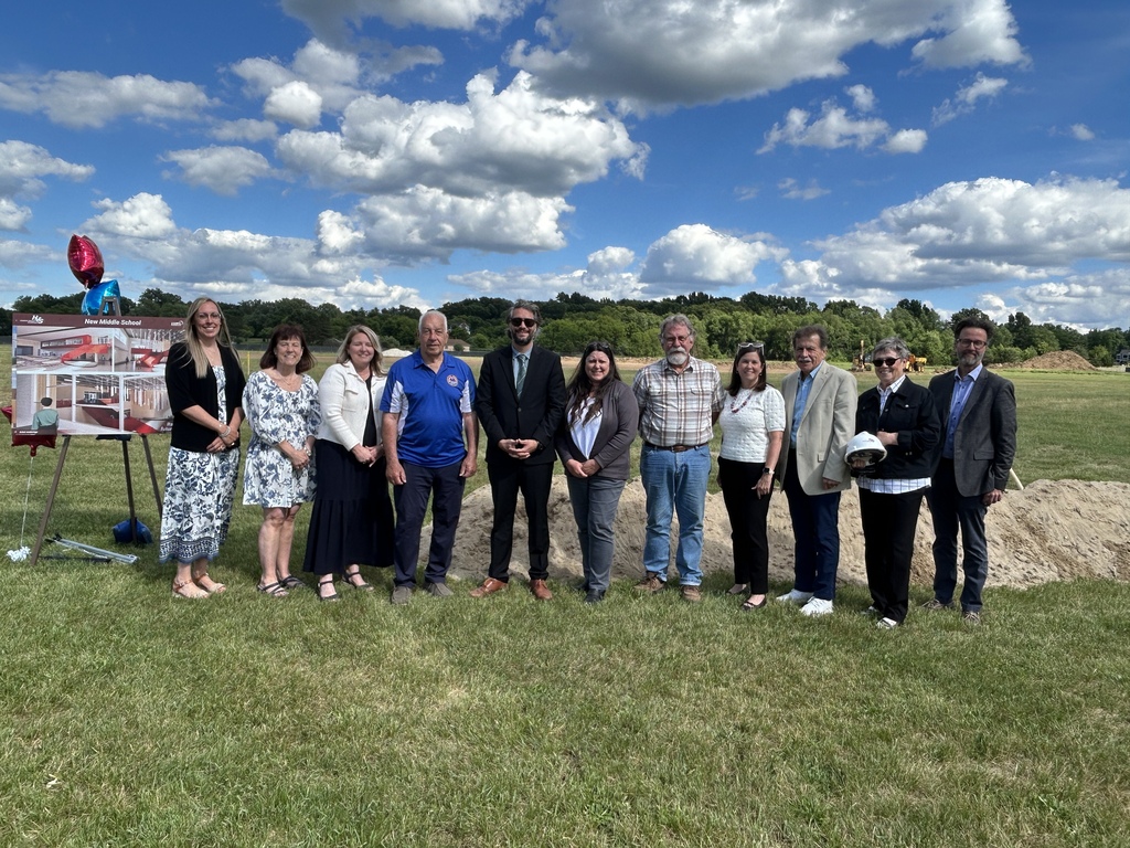 Photo of several people posing for a photo  standing in front of a mound of dirt