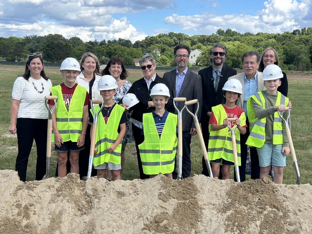 Photo of several people posing for a photo, some of them with hard hats on, standing behind a mound of dirt