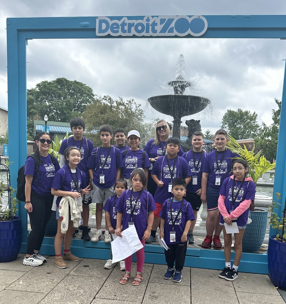 Several children and two women  smiling and posing for a photo in front of a Detroit Zoo sign