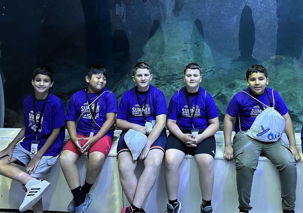 5 boys  smiling and posing for a photo in front of a large aquarium 