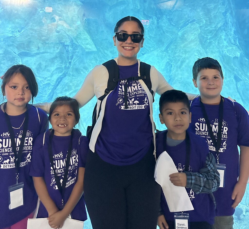 Several child and a woman  smiling and posing for a photo in front of a large aquarium 