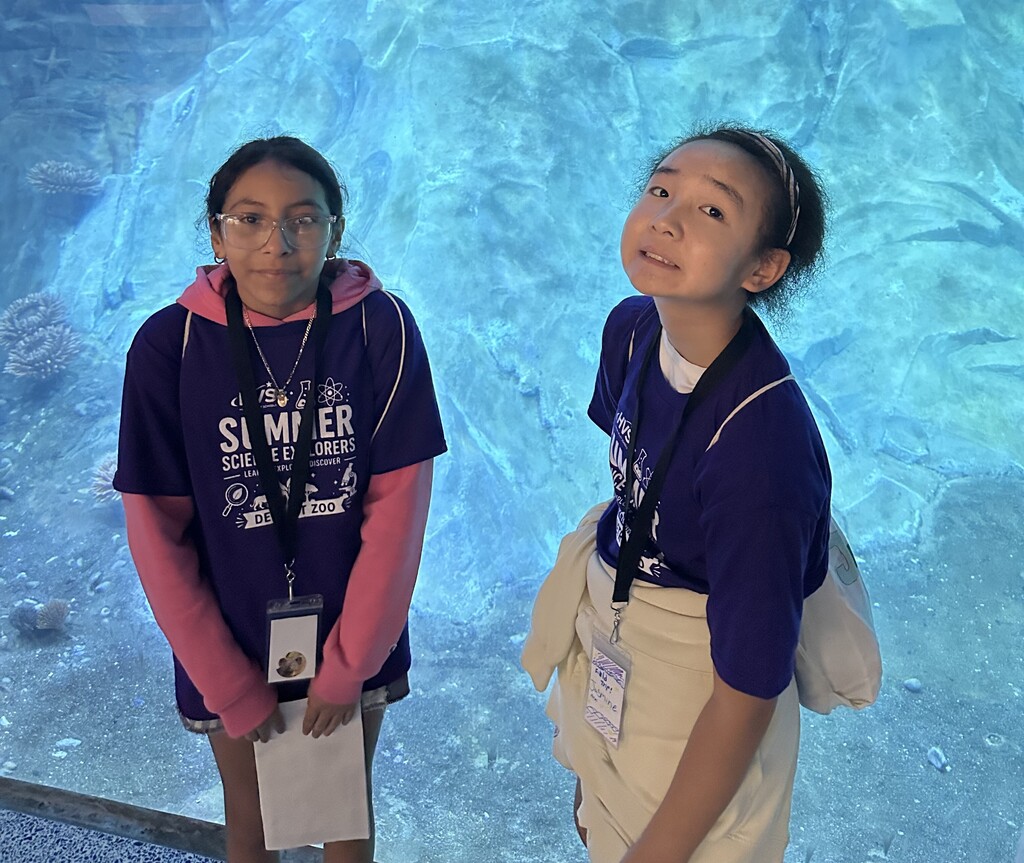 Two girls smiling and posing for a photo in front of a large aquarium 