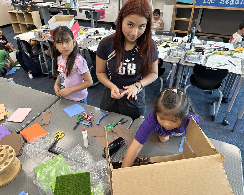 Three kids working on crafts at a large table 