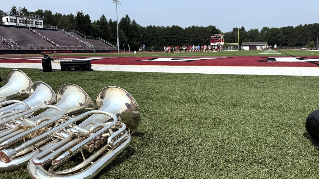 photo of marching band instruments on the field while members stand in the distance