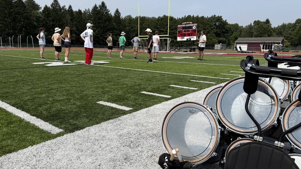 photo of marching band instruments on the field while members stand in the distance