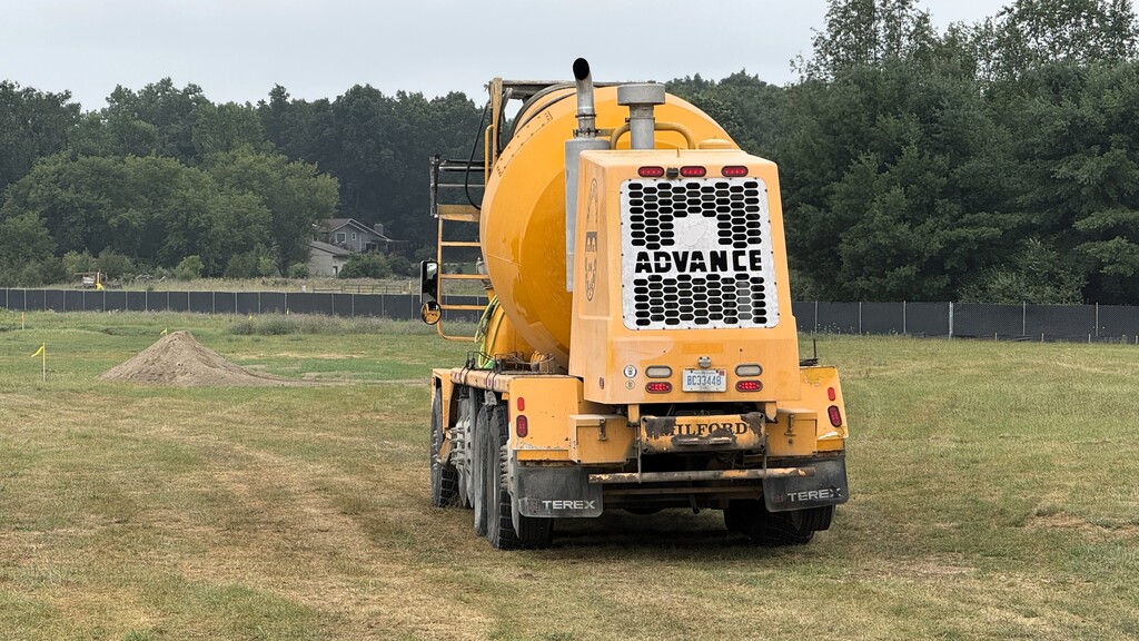 Photo of cement truck parked on a grass field near a constuction site