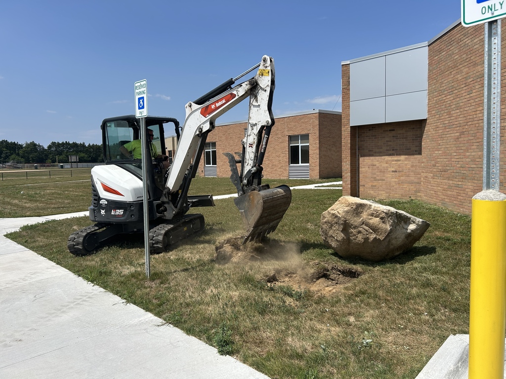 Photo of excavator digging a hole on grass outside a building