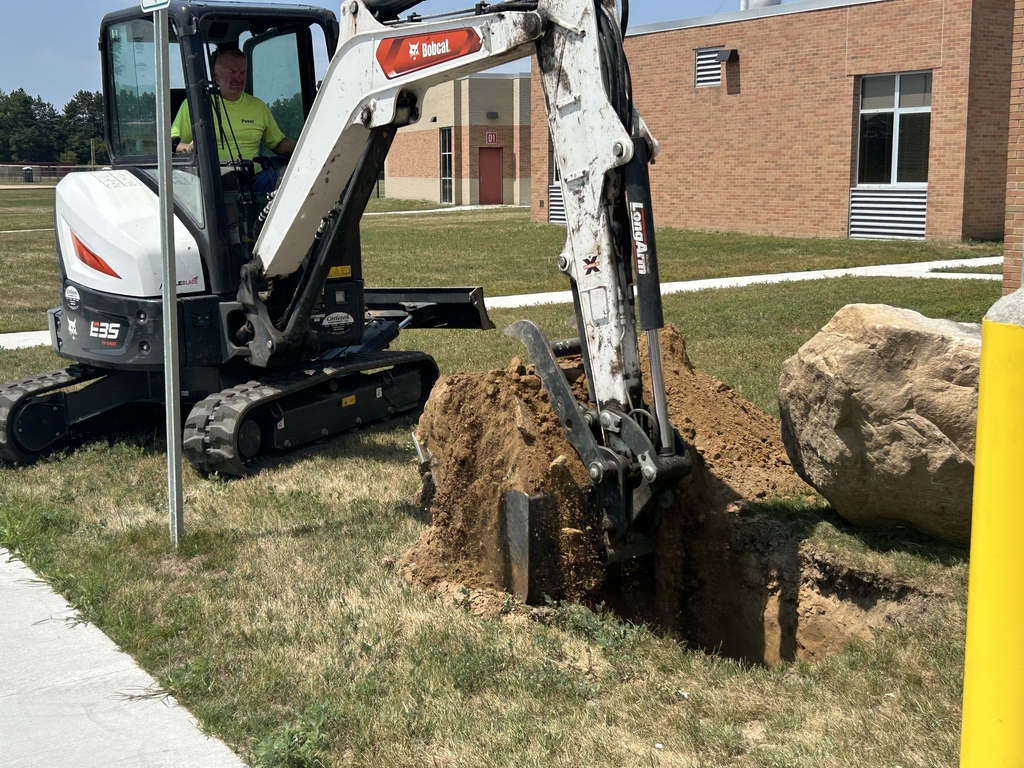 Photo of excavator digging a hole on grass outside a building