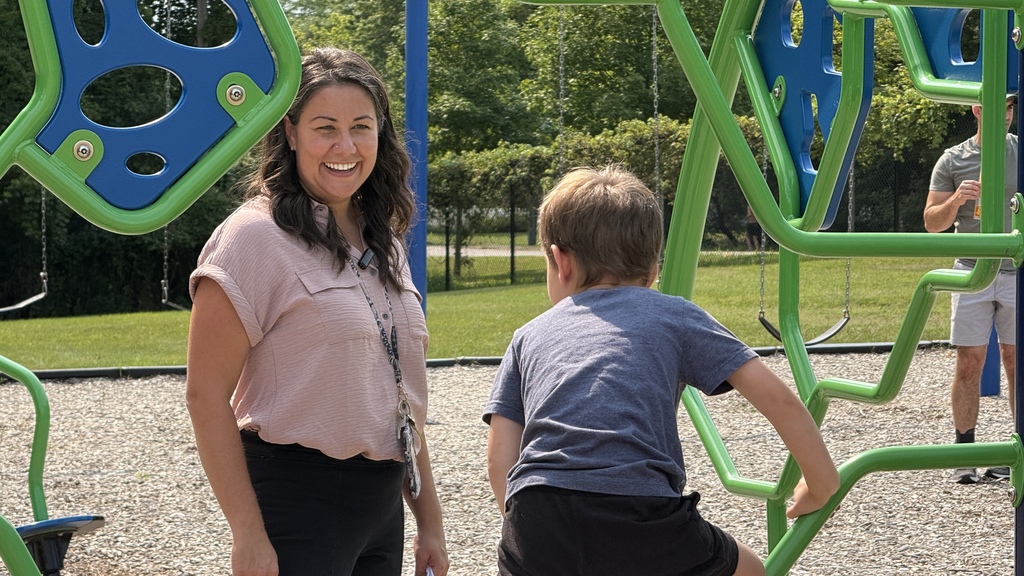 Woman smiling watching boy climb on playground equipment
