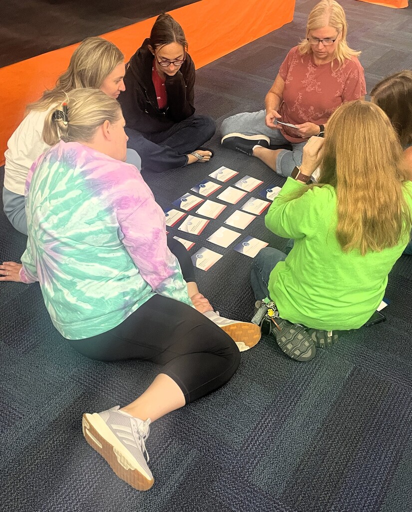 Photo of several women in a classroom setting sitting on the floor playing with several cards laid out in front of them