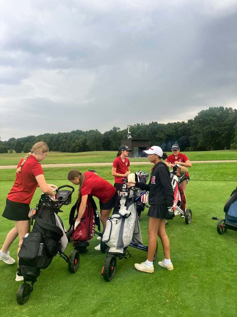 5 girls on a golf course surrounded by golf pull carts