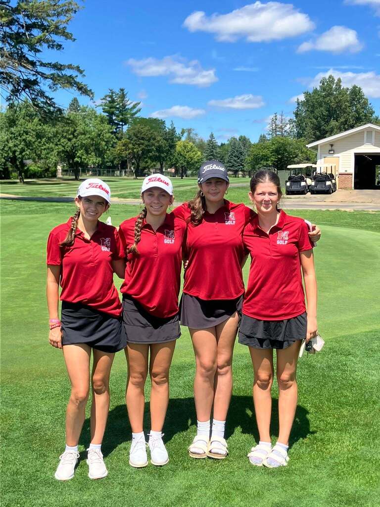 4 girls posing and smiling for a photo on a golf course in red shirts