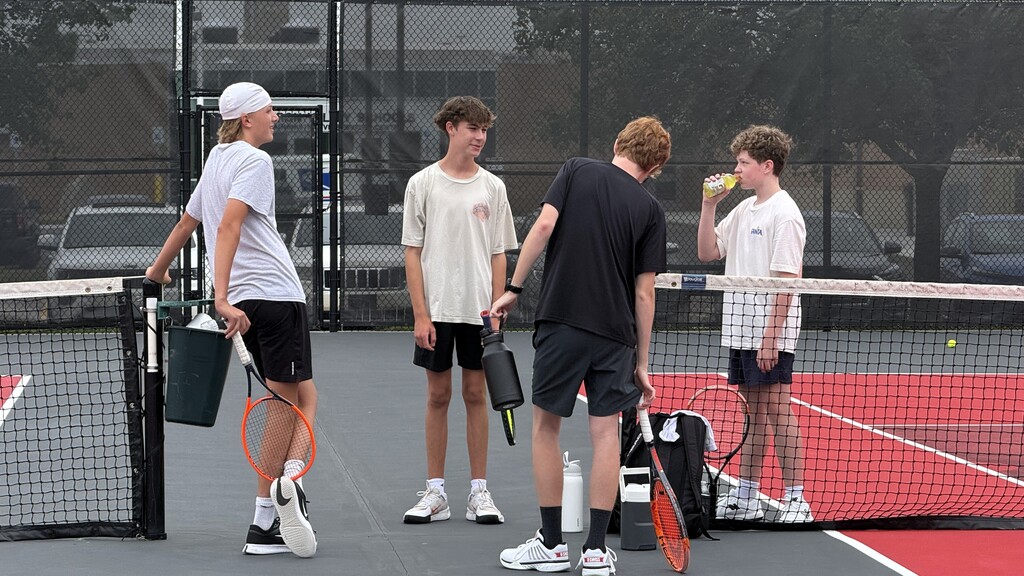 4 boys standing and talking to each other on a tennis court