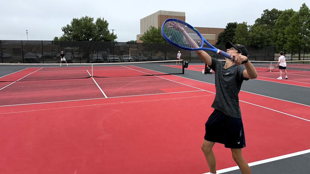 Boy serving and ready to hit a tennis ball over a net to another boy