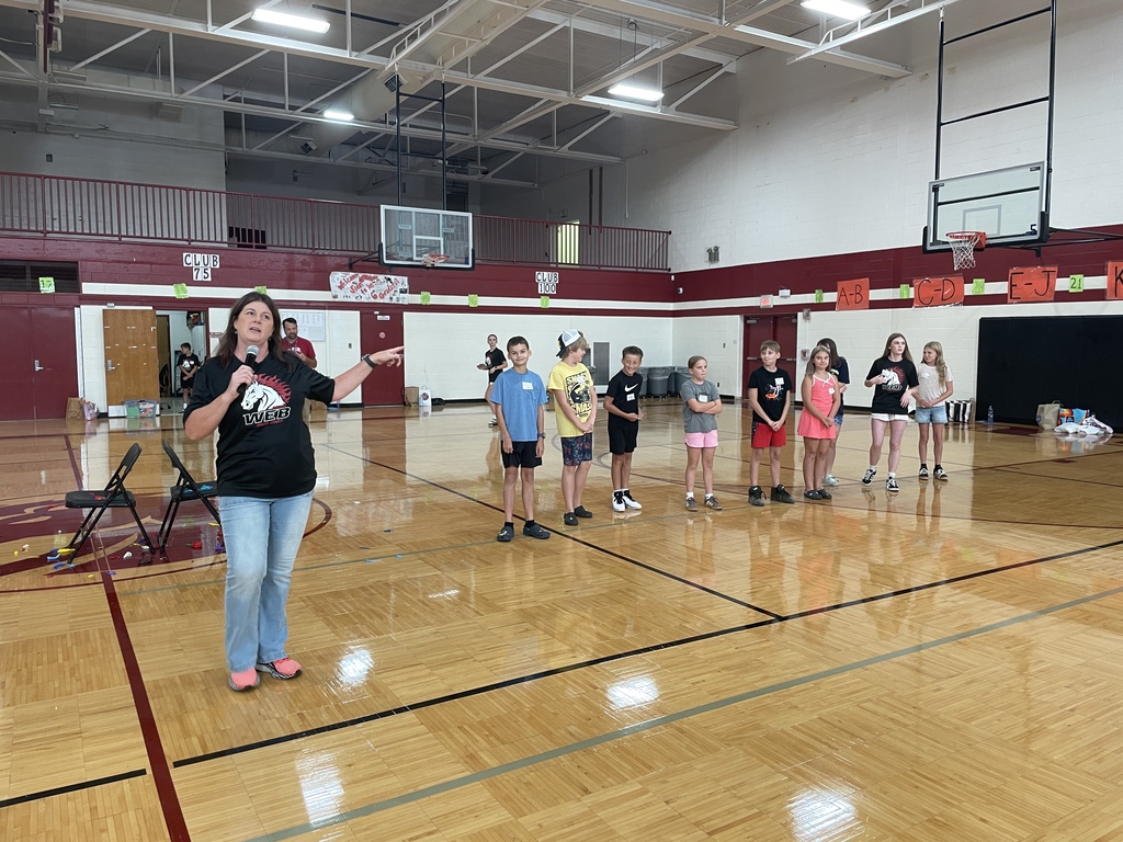 Adult speaking with kids/students standing behind her in a gym
