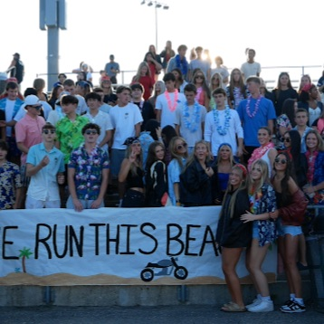 students sitting in a on the bleachers cheering on a football team