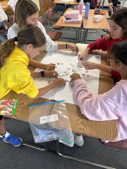 Students work as a group to solve a puzzle on their desks.