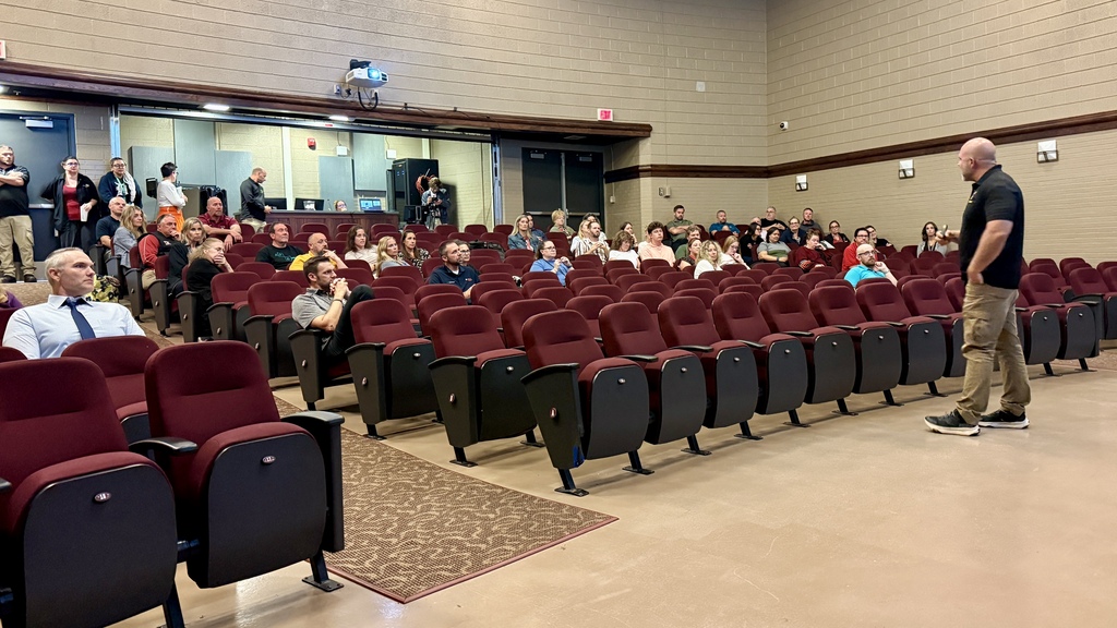 Several teachers sitting in an auditorium listening to man speak