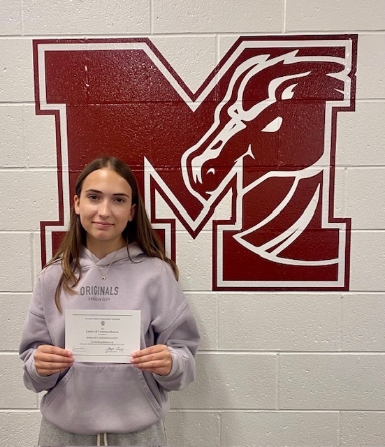 Photo of female student holding a certificate in front of an M logo
