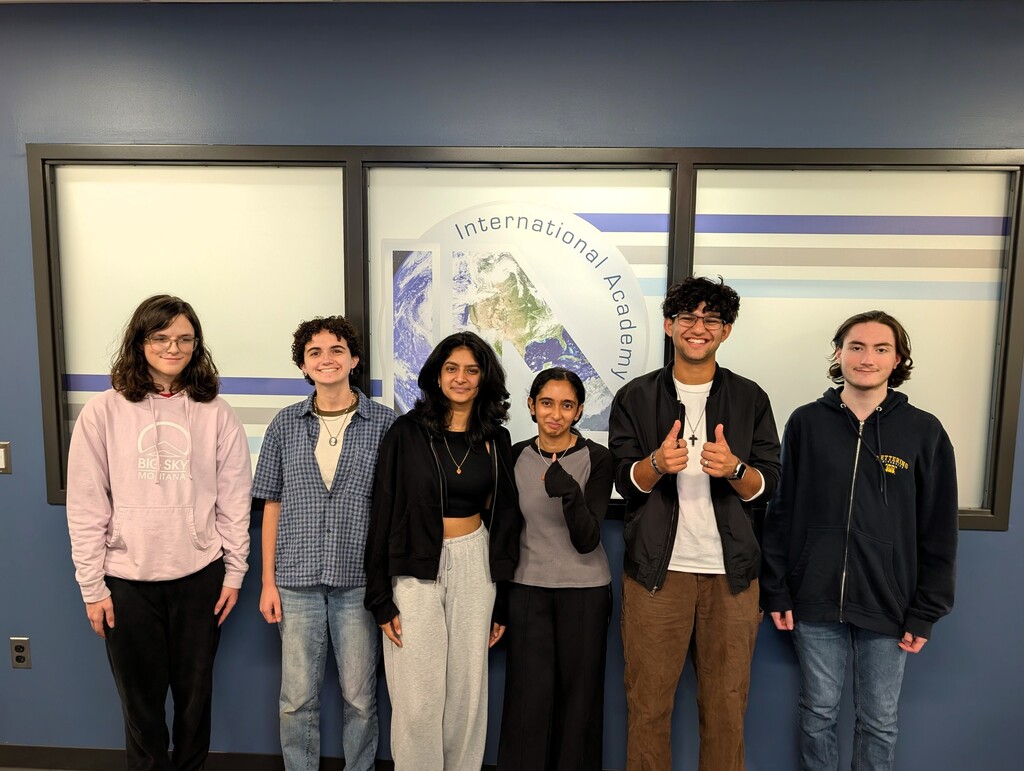 Photo of 6 students posing for a photo in front of an IAW sign