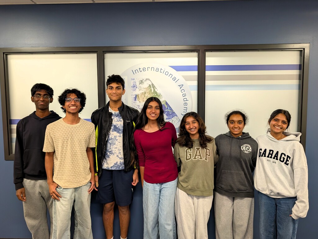 Photo of 7 students posing for a photo in front of an IAW sign