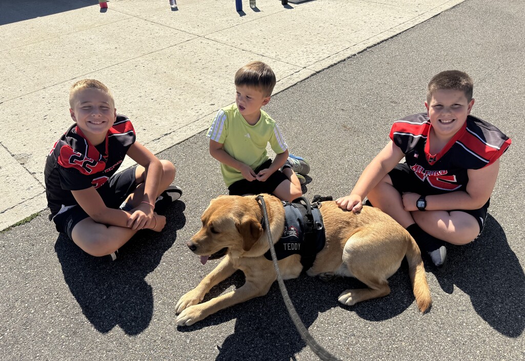 4th grade students with kindergarten students on the playground with the theray dog.