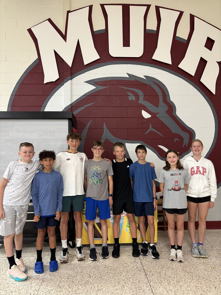 Eight mountain bike racing students stand together in front of the Muir logo with a colt