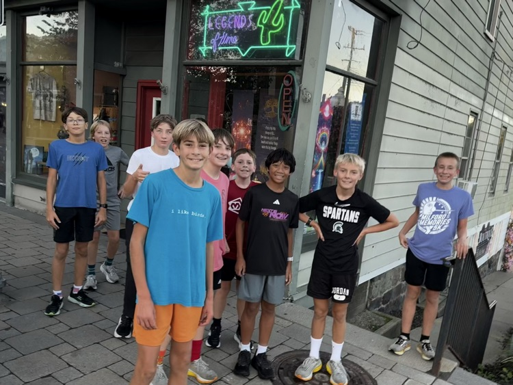Cross country runners stop before a crosswalk to smile in Milford