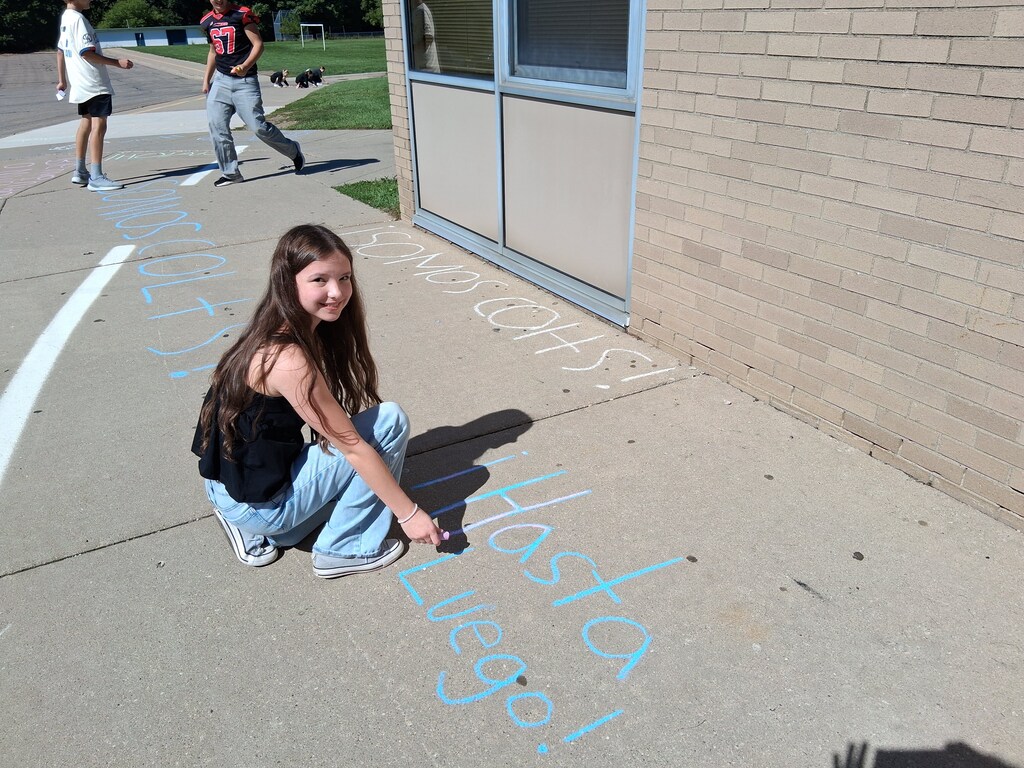 Student writing Hasta Luego with blue sidewalk chalk