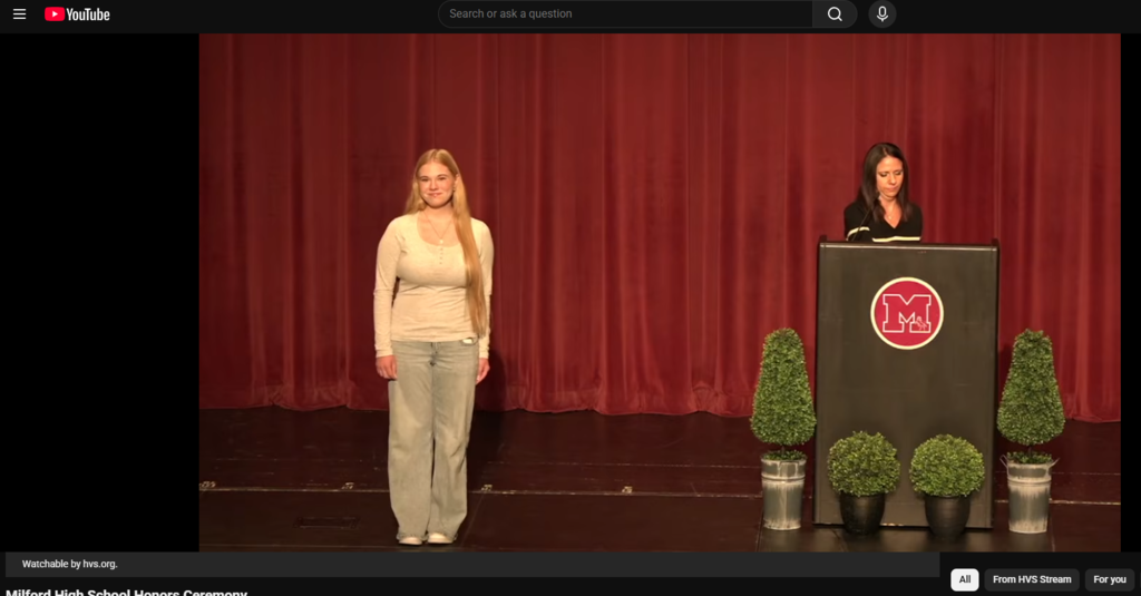 Photo of student standing on stage smiling next to a woman at a podium