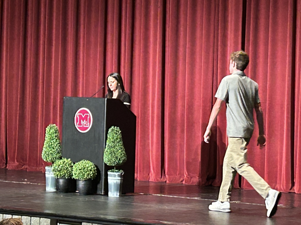 Teen walking on a stage looking at a woman at a podium in a theatre