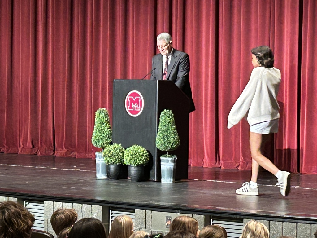 Teen walking on a stage looking at a man at a podium in a theatre