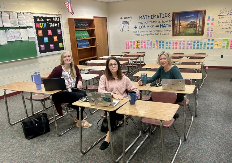 three teachers sit in desks with laptops 