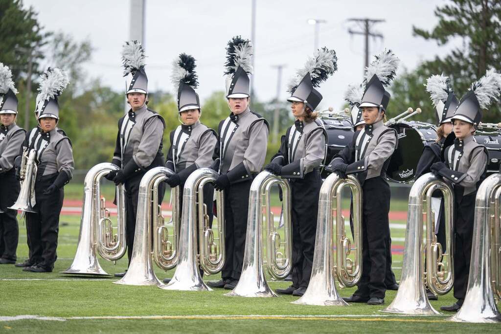 Several band members standing on a football field all wearing black and grey uniformsor practice.